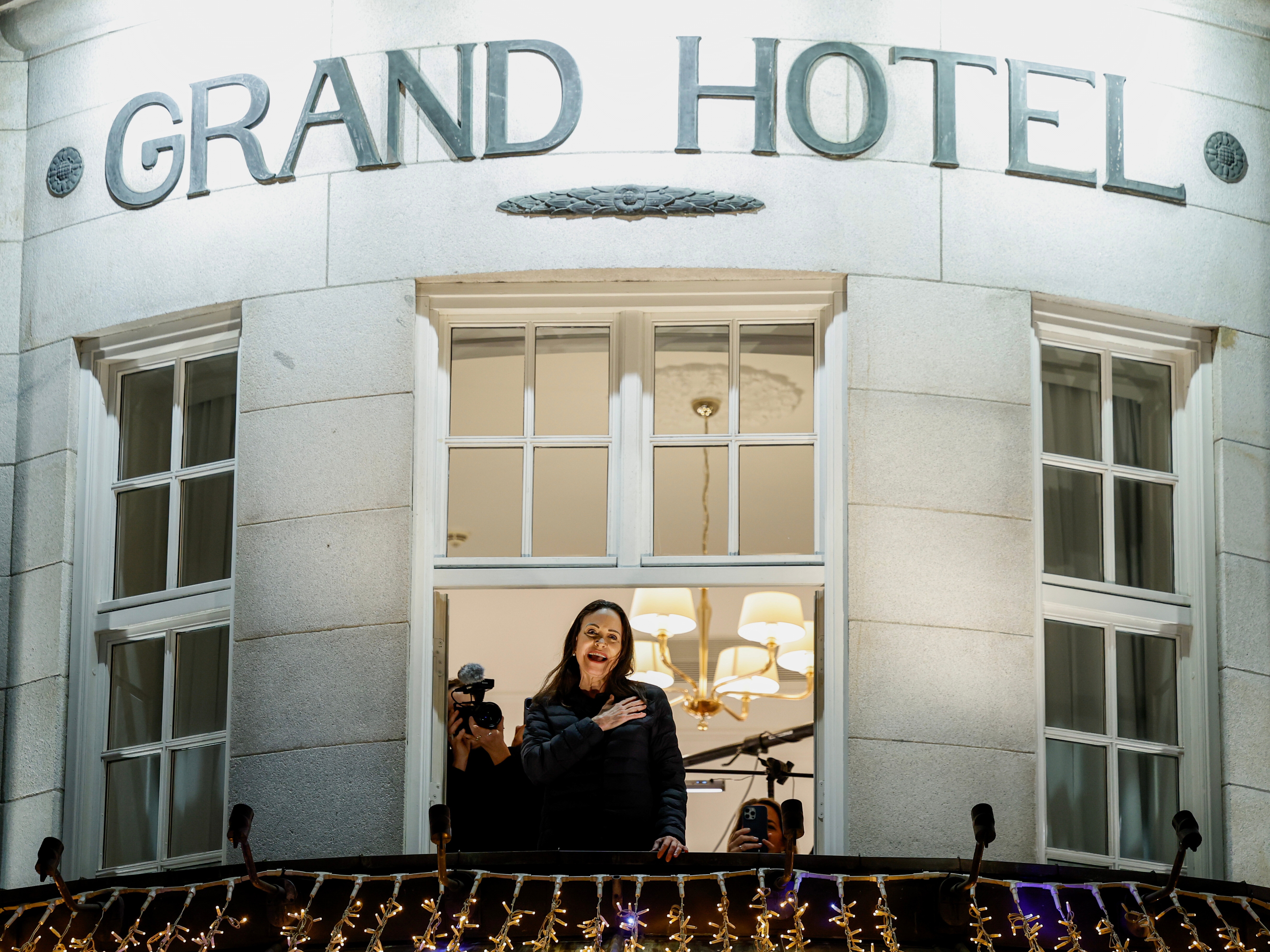 caption: Nobel Peace Prize laureate Maria Corina Machado reacts to the crowd gathered below from a balcony at the Grand Hotel, in Oslo, Norway, early Thursday.
