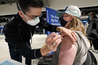 caption: Seattle Kraken fan Jami Lopez, right, of Bellevue, Wash., receives a Moderna coronavirus booster vaccine from health care worker Zach Hren at the arena before the Kraken's NHL hockey game against the St. Louis Blues, Friday, Jan. 21, 2022, in Seattle. The boosters were available to fans at the pop-up clinic at the Thursday and Friday Kraken games. 