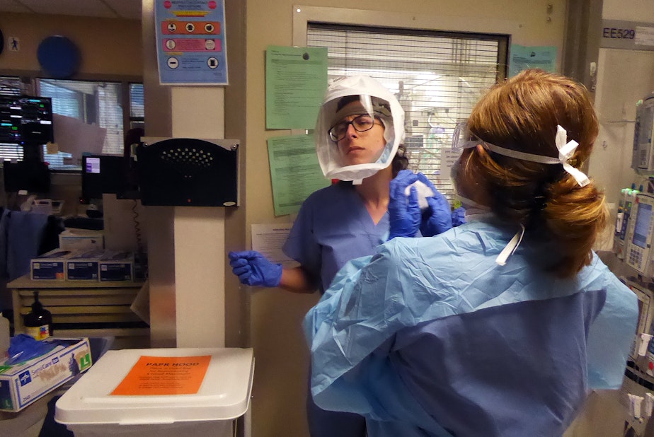 caption: Leah Silver, left, is a nurse on the Covid ICU at University of Washington Medical Center in Seattle on April 24, 2020. Ashlee Davis, also a nurse, assists her removal of personal protective equipment after she has been in a patient's room.