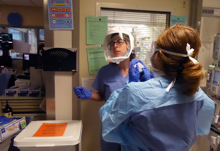 caption: Leah Silver, left, is a nurse on the Covid ICU at University of Washington Medical Center in Seattle on April 24, 2020. Ashlee Davis, also a nurse, assists her removal of personal protective equipment after she has been in a patient's room.