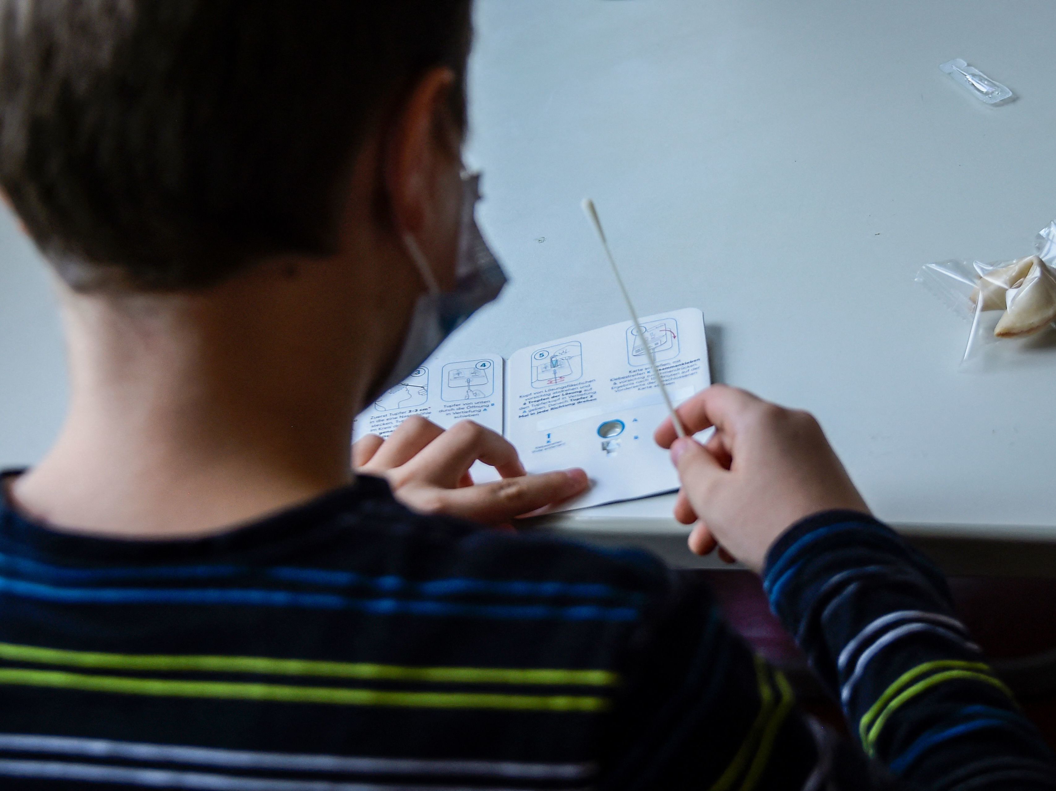 caption: A pupil wearing a face mask reads instructions for a coronavirus rapid test kit at the start of a lesson at an elementary school in Berlin on August 9, 2021.