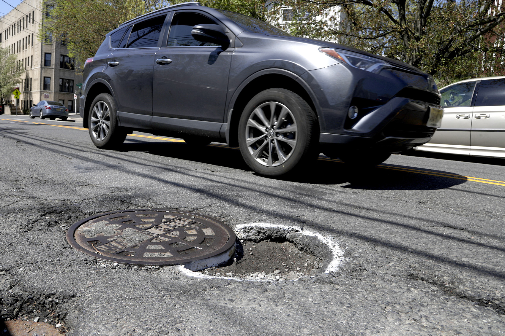 caption: A vehicle maneuvers around a pothole outlined by paint near a manhole along Summit Avenue, Tuesday, April 23, 2019, in Jersey City, N.J. (Julio Cortez/AP)