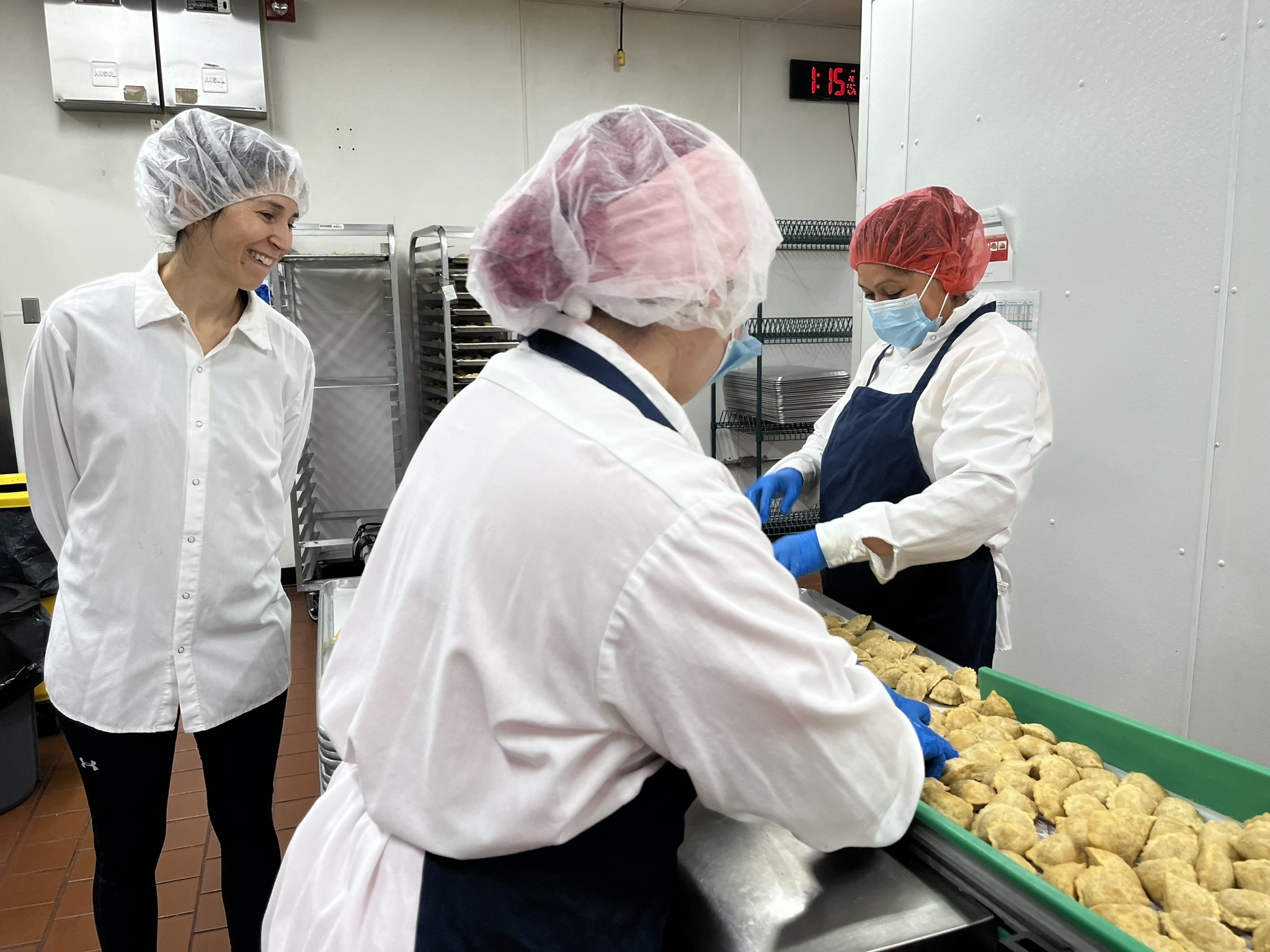 caption: Margarita Womack, owner of the frozen empanadas company MasPanadas, (left,) looks over staffers inspecting empanadas to ensure quality control. Imperfect empanadas such as those with an uneven shape are removed and donated.