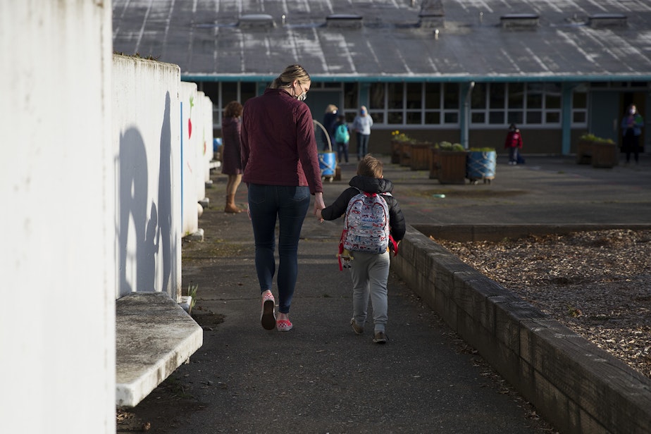 caption: Shelly Kuntz, left, and August Kuntz, right, a kindergarten student at Northgate Elementary School, walk together while holding hands on Monday, April 5, 2021, on the first day of in-person learning at the school in Seattle.