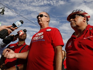 caption: United Auto Workers President Shawn Fain talks with the news media before marching in the Detroit Labor Day Parade on September 4, 2023 in Detroit, Michigan.