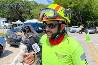 caption: Moises Soffer, a volunteer member of Cadena International's search-and-rescue team working at the site of the condo building collapse, holds a trained search dog named Oreo in Surfside, Fla., on Sunday.