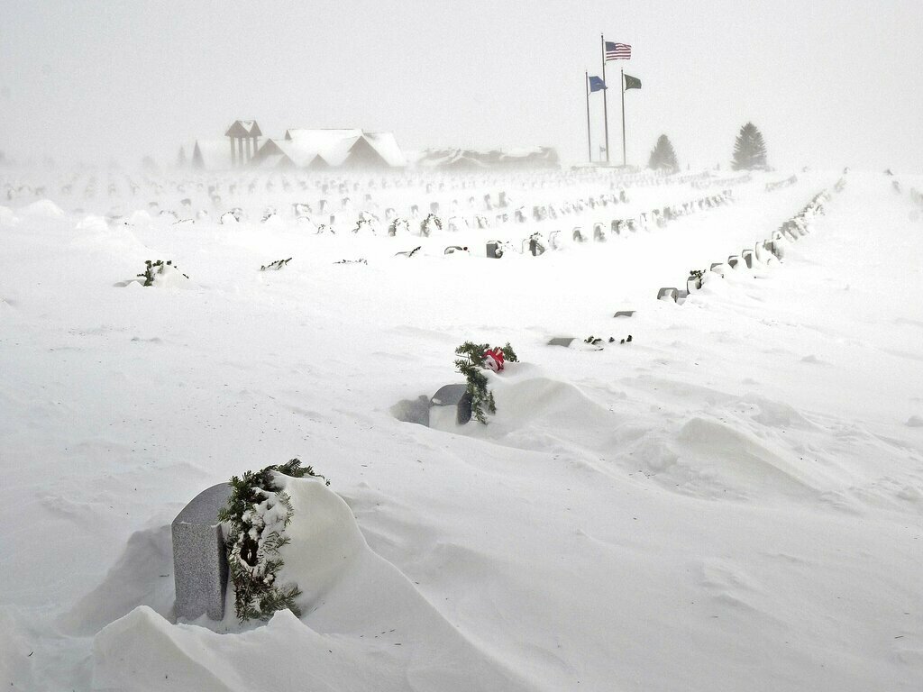 caption: Rows of headstones at the North Dakota Veterans Cemetery are blanketed Thursday by drifting snow in Mandan, N.D.