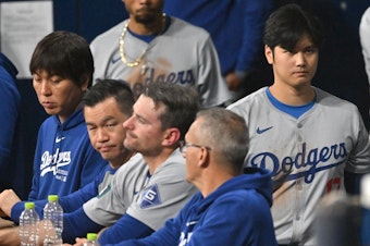 caption: Baseball star Shohei Ohtani (right) and his interpreter, Ippei Mizuhara (left), are seen in the dugout in the 2024 MLB Seoul Series game between the Los Angeles Dodgers and the San Diego Padres. The Dodgers have fired Mizuhara after Ohtani's representatives claimed he was the victim of "a massive theft."