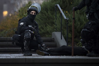 caption: A Seattle police officer holds down the feet of an individual who was arrested during the sweep of unhoused community members at Cal Anderson Park  on Friday, December 18, 2020, in Seattle. 