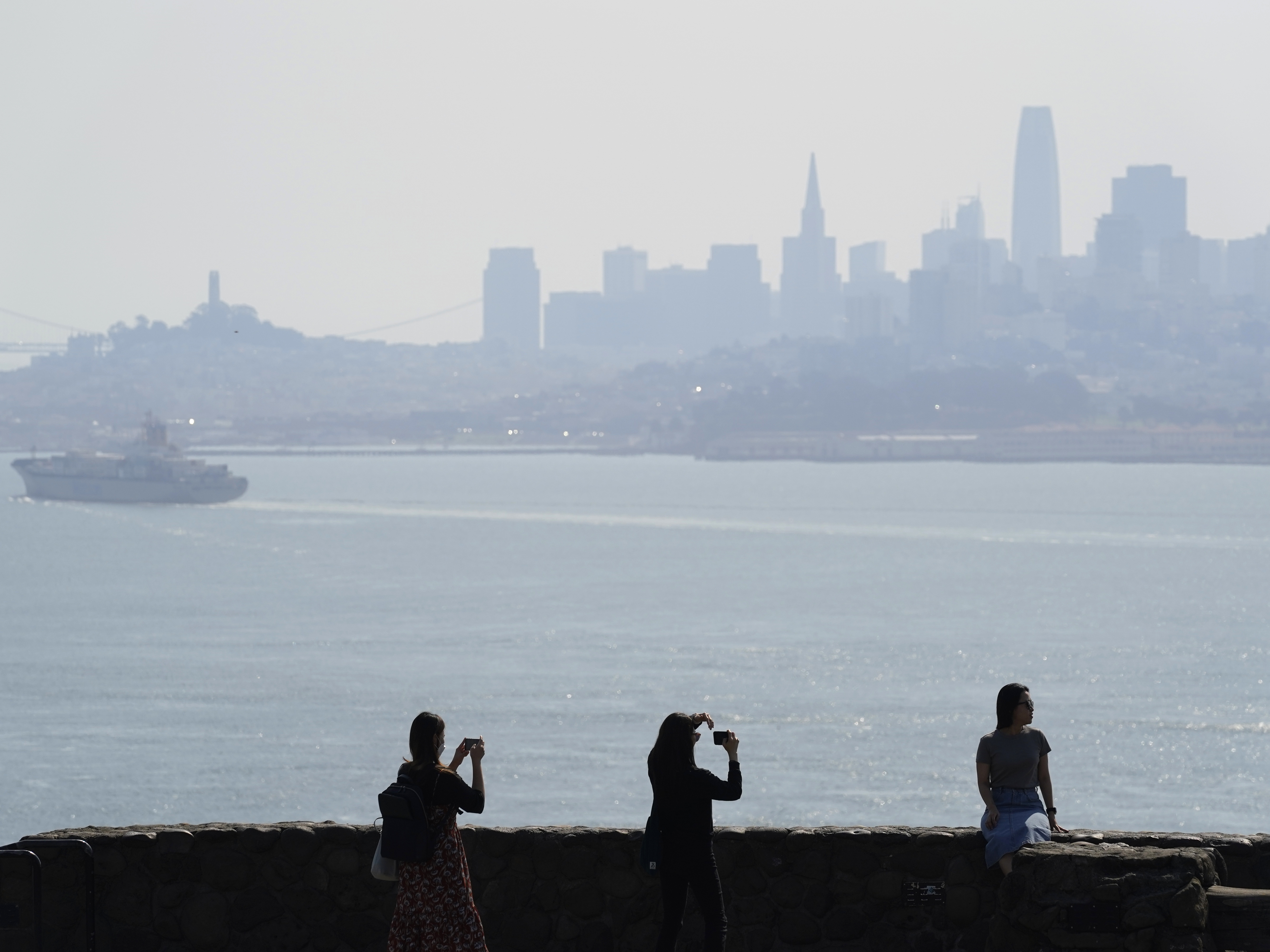 caption: People take pictures at a vista point with the San Francisco skyline obscured by smoke from wildfires during a spate of smoke during 2020, one of the worst wildfire smoke years on record.