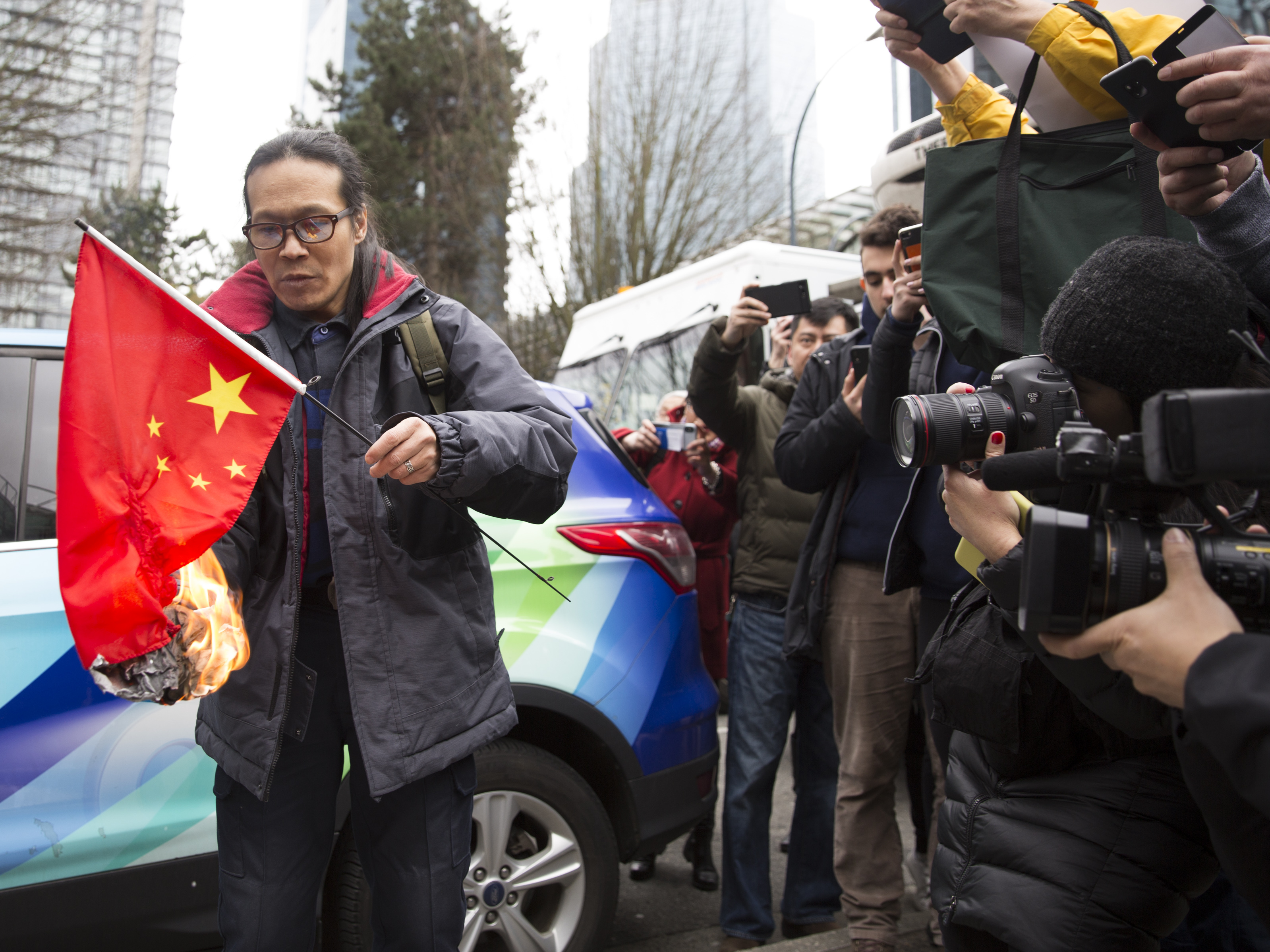 caption: Kuang Yang burns a Chinese flag to protest human rights abuses, outside British Columbia Supreme Court in Vancouver on March 6, as Huawei Chief Financial Officer Meng Wanzhou appears in court.