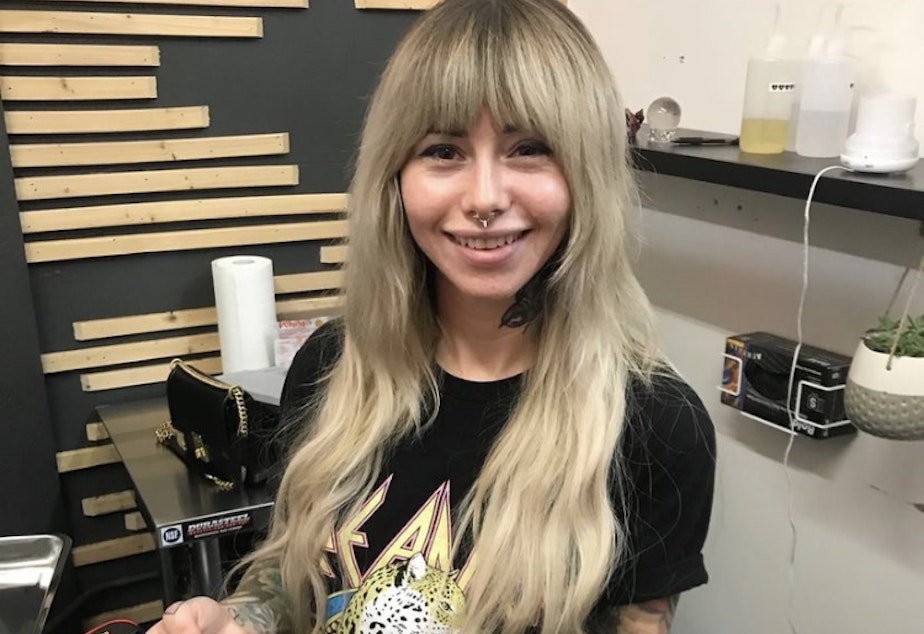 caption: Tattoo artist Nikki Stoops holds up two tattoo needles.