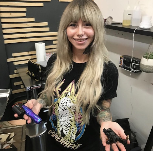 caption: Tattoo artist Nikki Stoops holds up two tattoo needles. 