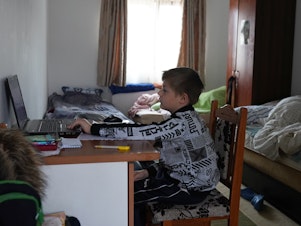 caption: Dima, who fled the war in Ukraine with his mother, attends an online class, at the "Saint John the Baptist" Monastery in Ruscova, where 12 Ukrainians are currently being hosted, on March 30, 2022 in Ruscova, Romania.