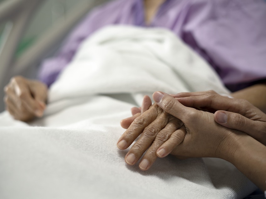 A daughter holds her mother's hand and encourages her while sitting on a hospital bed.