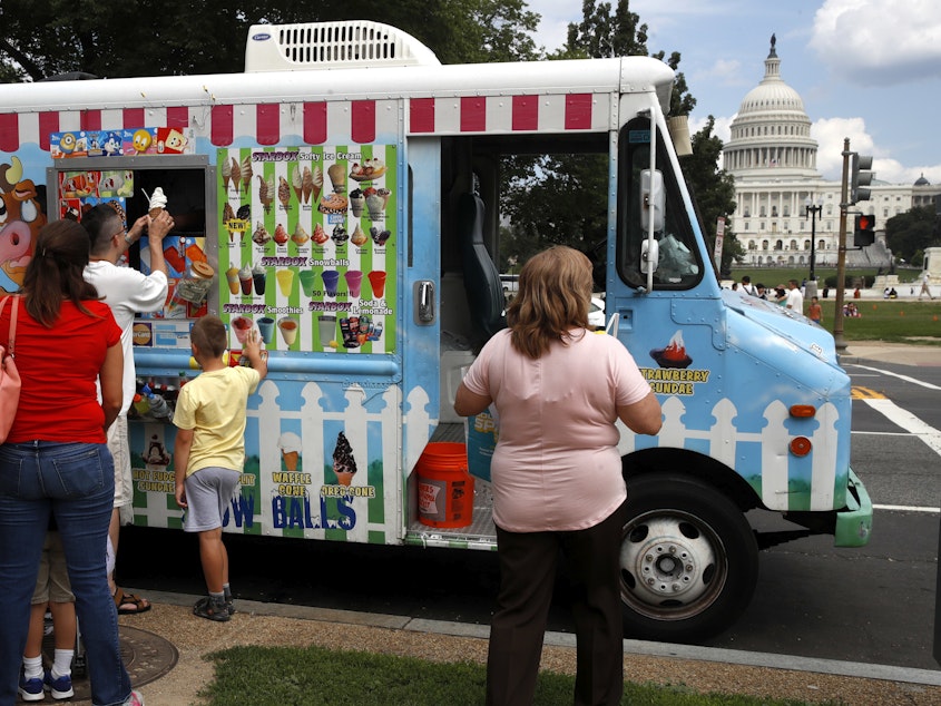 caption: With the U.S. Capitol as a backdrop, tourists wait in line to get ice cream from a food truck on the National Mall in Washington.