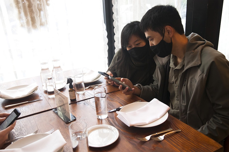 caption: Julie Ding and James Che, right, look at a QR code menu on their phones before ordering on Wednesday, October 21, 2020, at Spinasse on Capitol Hill in Seattle. “We’re expected to sort of enforce those rules and so in addition to everything that comes with running a restaurant, now you have this extra layer of added stress," said general manager Angela Lopez. "We’re here putting ourselves at risk just by being at work."