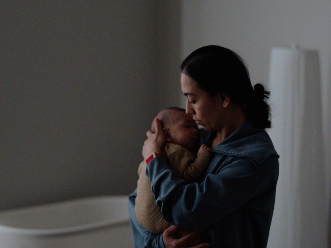 caption: Farida Azizova-Such inside the nursery rocking her son to sleep. "He was 5 weeks when we started coming. It's just my husband and I taking care of him, so I was alone at home. I wanted to find new moms to connect with and a safe space to be able to come and learn about how to take care of a baby, and also my identity shifted when you become a mother."