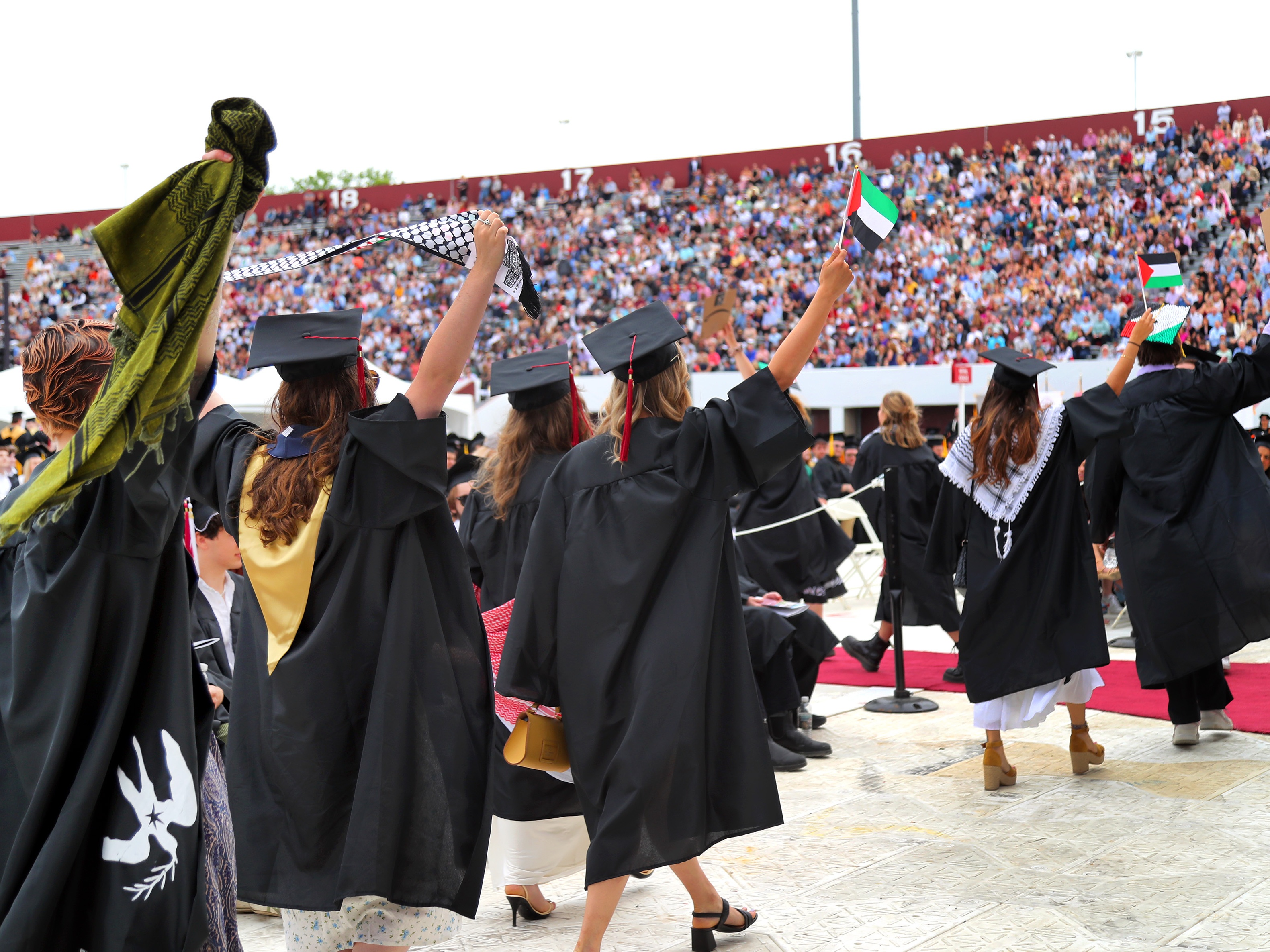 caption: Pro-Palestinian students hold up Palestinian flags during UMass Amherst graduation ceremonies in May 2024. They left the graduation event in protest.
