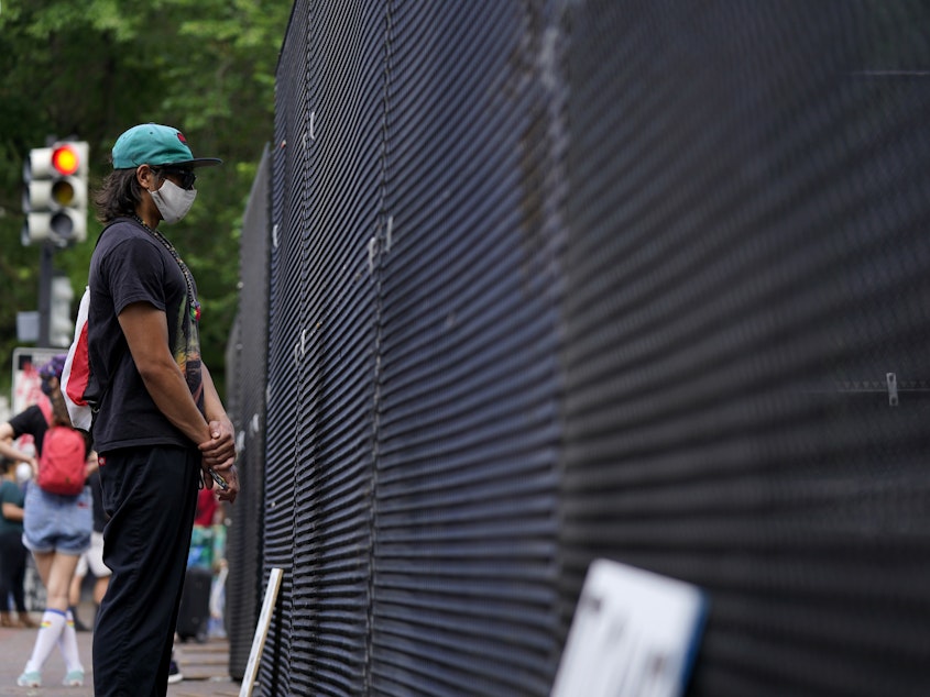 caption: A person stands next to a fence as demonstrators protest Thursday near the White House over the death of George Floyd. The security perimeter is being extended several blocks.
