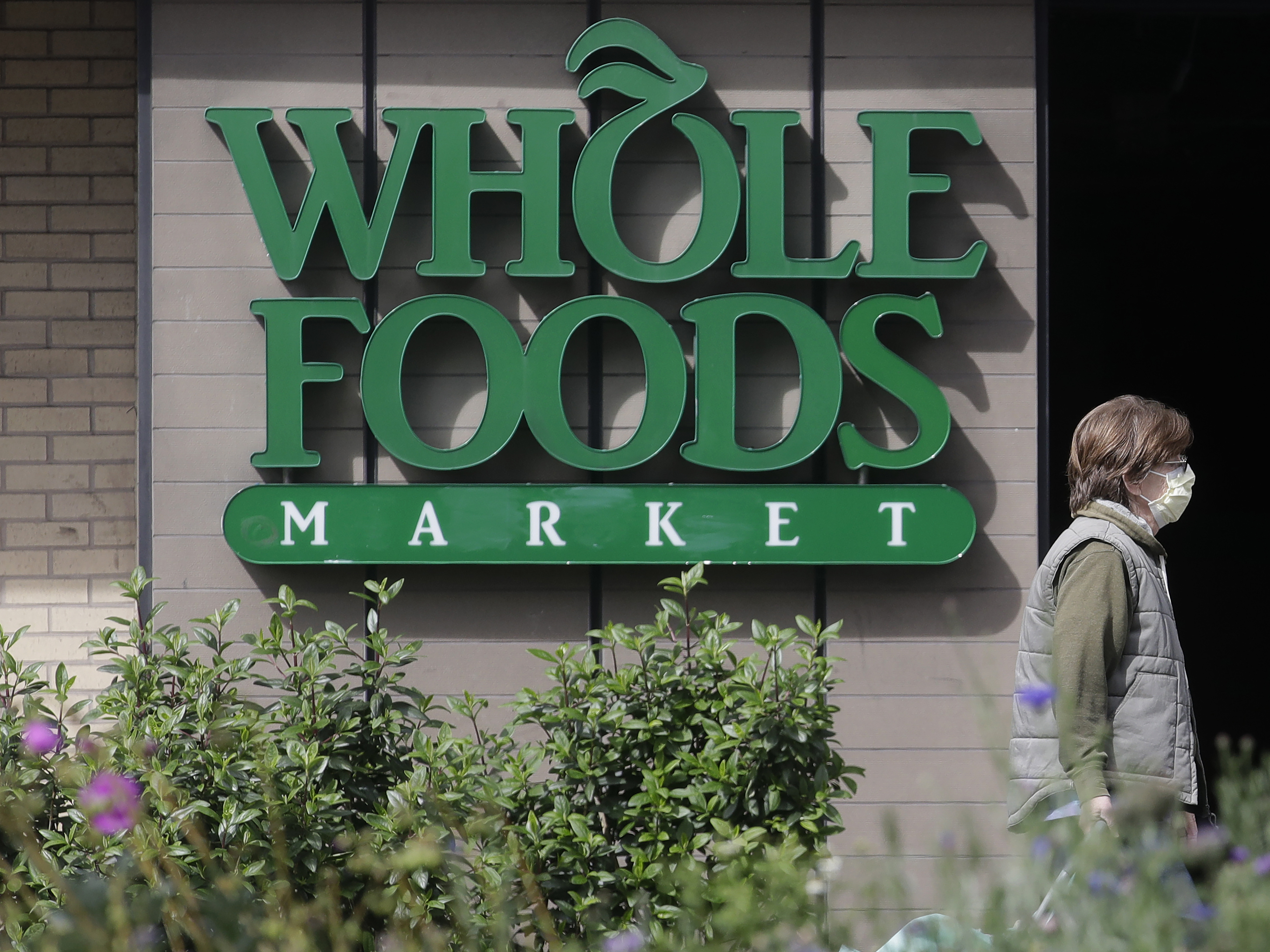 caption: A pedestrian wears a mask while walking past a sign for a Whole Foods Market in San Francisco, Tuesday, March 31, 2020.