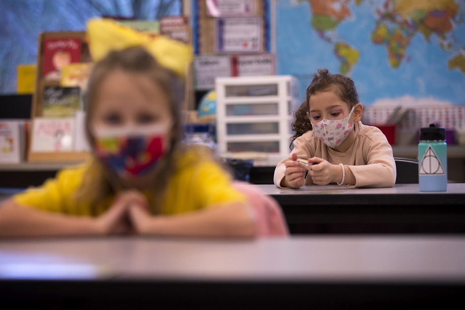 caption: Second-grade student Nelly, right, plays with a bottle of hand sanitizer at her desk on Thursday, January 21, 2021, as second-grade students returned to in-person learning at Somerset Elementary School in Bellevue. 
