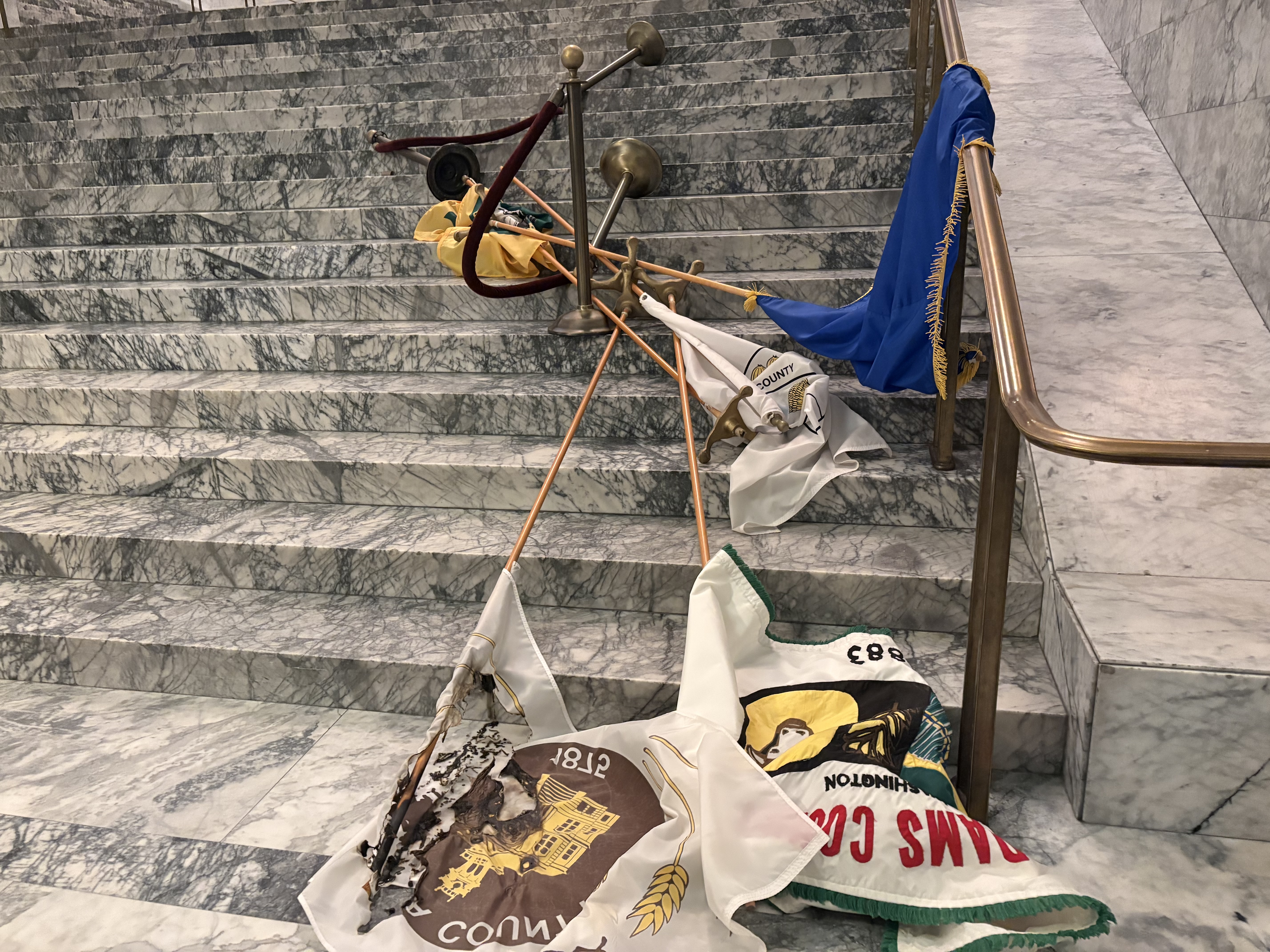 caption: County flags burned and thrown by an intruder in the state capitol's Legislative Building on October 5, 2025.