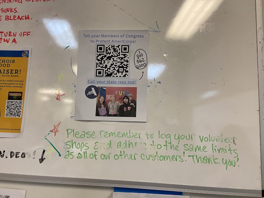 caption: A printed sign at the University District Food Bank in Seattle urges readers to contact lawmakers about the funding cuts to AmeriCorp.