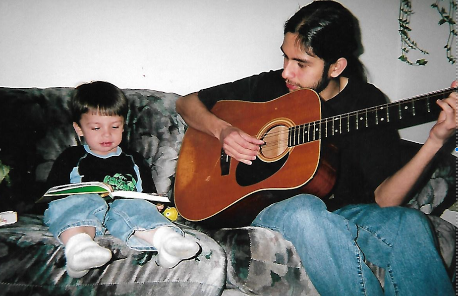 caption: Hugo Guerra plays a song on the guitar as he helps his son Adrian read a book.