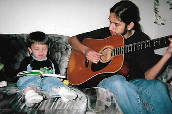 caption: Hugo Guerra plays a song on the guitar as he helps his son Adrian read a book.