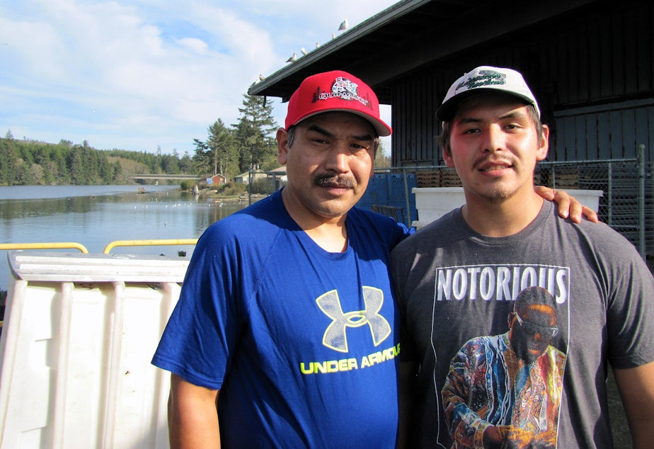 caption: Shane Underwood (left) and his son, David, stand at the Quinault Indian Nation’s seafood plant in Taholah, Washington. The loss of the largest glacier that feeds the Quinault River and rising seas are threatening the tribe’s way of life.
