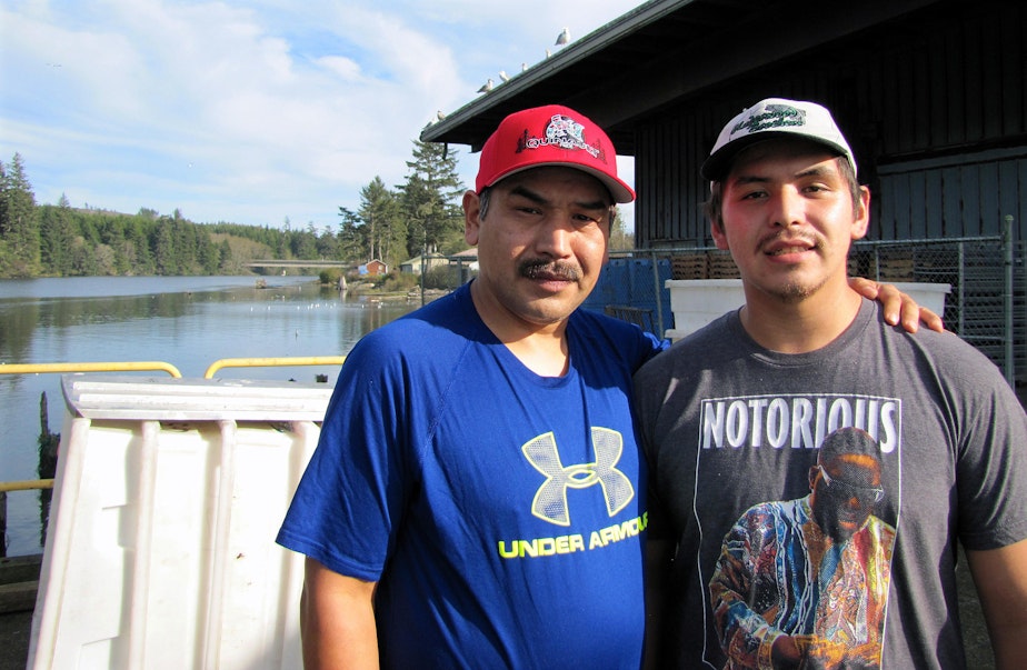 caption: Shane Underwood (left) and his son, David, stand at the Quinault Indian Nation’s seafood plant in Taholah, Washington. The loss of the largest glacier that feeds the Quinault River and rising seas are threatening the tribe’s way of life.
