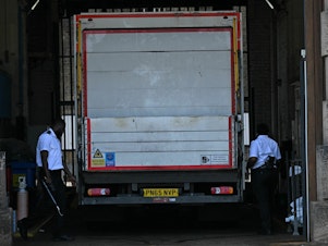 caption: Prison guards walk around the sides of a truck at the gates of Wandsworth Prison in south London on Thursday, a day after terror suspect Daniel Abed Khalife escaped from the prison. British authorities have issued an all-ports alert to track down Khalife, a former soldier awaiting trial on terrorism charges. He escaped from jail by clinging to the bottom of a delivery truck.