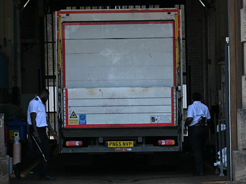 caption: Prison guards walk around the sides of a truck at the gates of Wandsworth Prison in south London on Thursday, a day after terror suspect Daniel Abed Khalife escaped from the prison. British authorities have issued an all-ports alert to track down Khalife, a former soldier awaiting trial on terrorism charges. He escaped from jail by clinging to the bottom of a delivery truck.