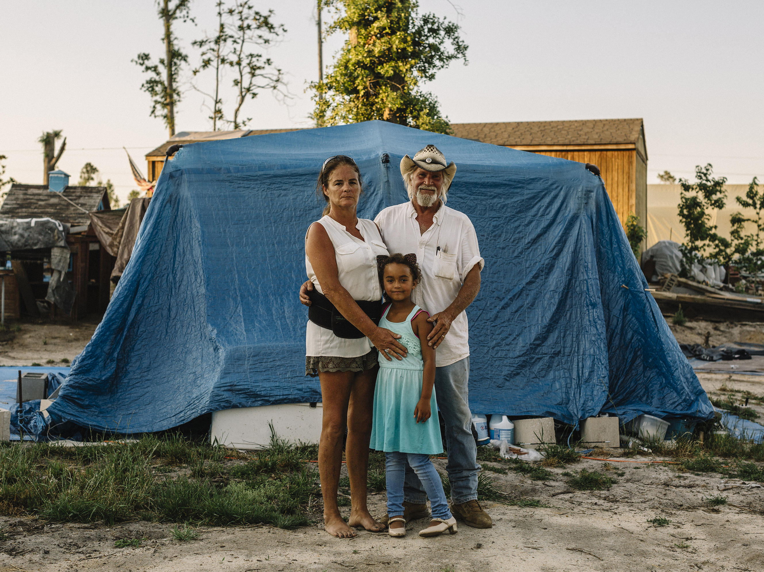 caption: Shelly and Sam Summers stand with daughter Gabby in front of a makeshift shelter on their rural Bay County property. They opened their backyard to people who were homeless after Hurricane Michael. At the peak, about 50 people lived there. Now, there are 18. "We still have our home," Shelly says. "They have nothing. So if we can at least offer them the comforts of home, it was worth it."