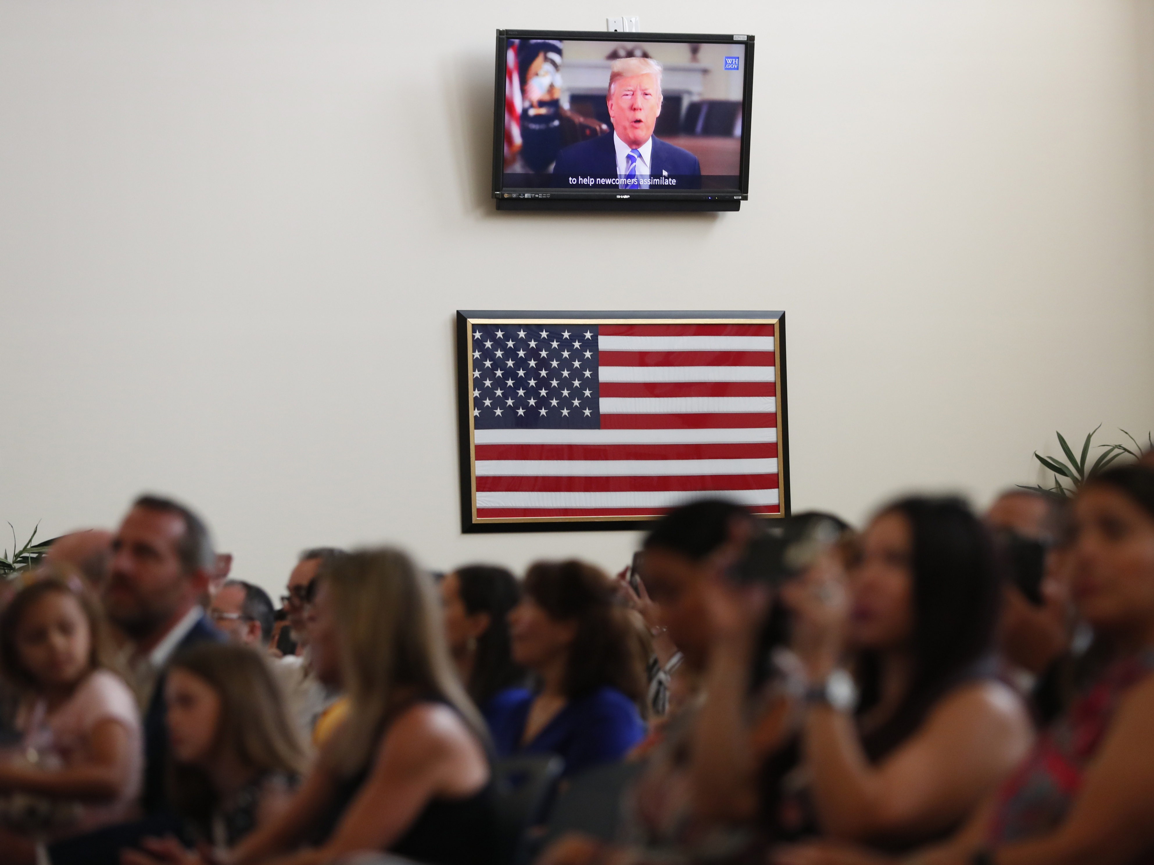 caption: A recorded video message by then-President Donald Trump plays at a 2019 naturalization ceremony for new U.S. citizens at the U.S. Citizenship and Immigration Services field office in Miami.