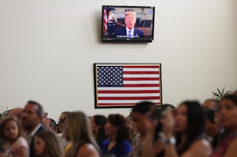 caption: A recorded video message by then-President Donald Trump plays at a 2019 naturalization ceremony for new U.S. citizens at the U.S. Citizenship and Immigration Services field office in Miami.