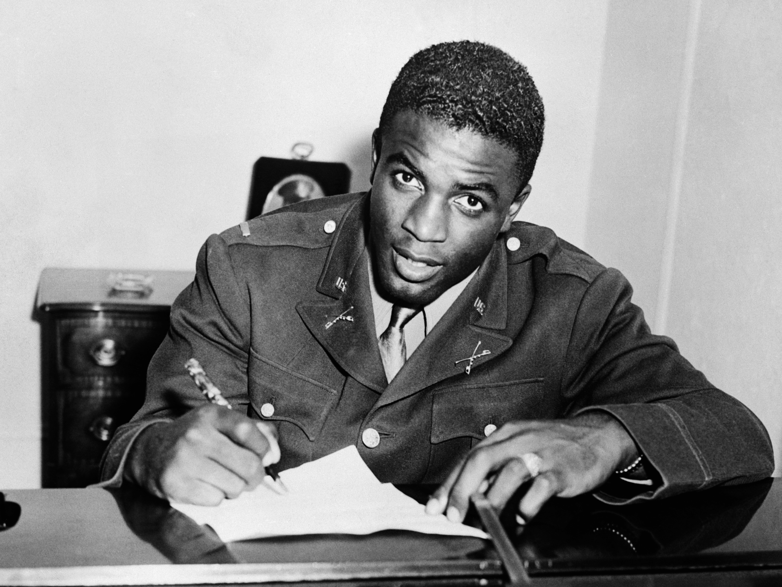 caption: Jackie Robinson, shown here in military uniform signing a contract with a farm team for the Brooklyn Dodgers, is among the veterans whose Department of Defense webpages were removed — and then restored — as part of the Trump administration's scrubbing of references to DEI material.