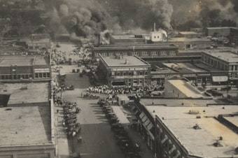 caption: This archival photo shows crowds of people watching fires during the June 1, 1921, Tulsa Race Massacre.