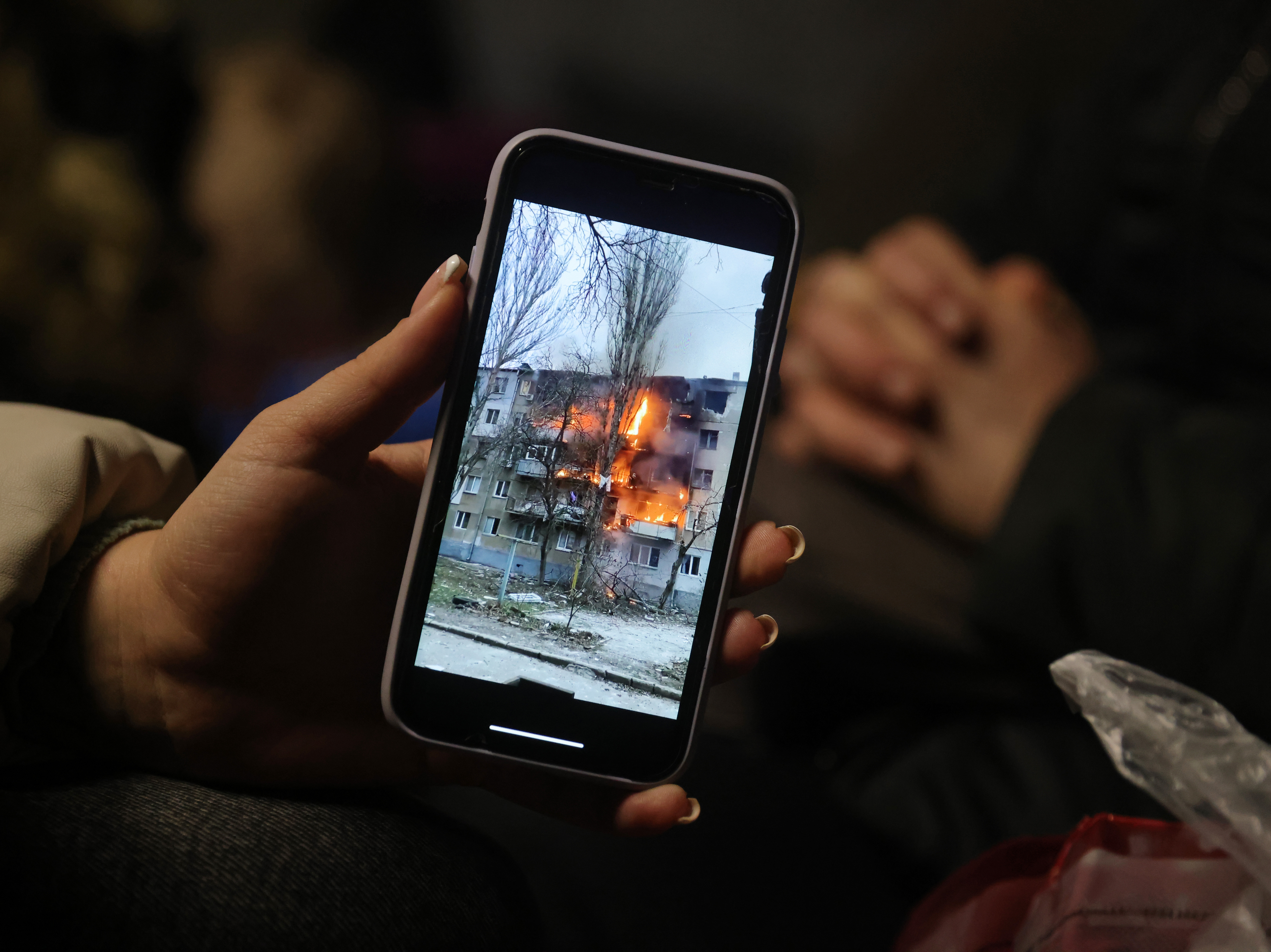 caption: Iryna Holoshchapova, a Ukrainian refugee who fled the embattled city of Mykolaiv, shows a video on her smartphone of an apartment block on fire following a Russian attack.