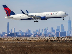 caption: A Boeing 767 passenger aircraft of Delta Air Lines arrives from Dublin at JFK International Airport in New York as the Manhattan skyline looms in the background on Feb. 7, 2024.