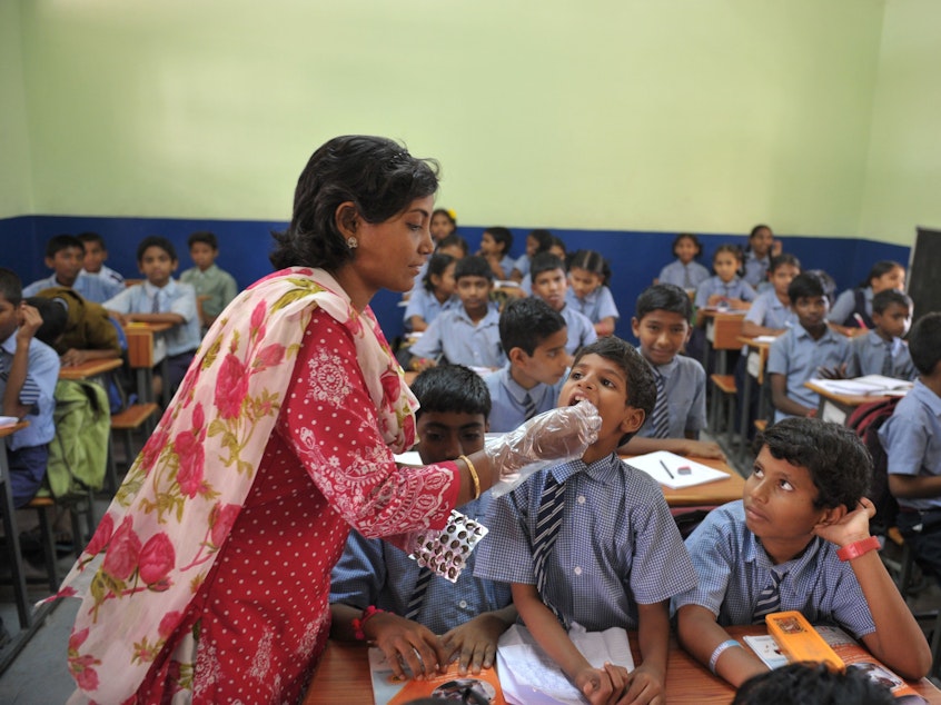 caption: A teacher gives a deworming tablet to a student during National Deworming Day at a high school in Hyderabad, India, in 2017.