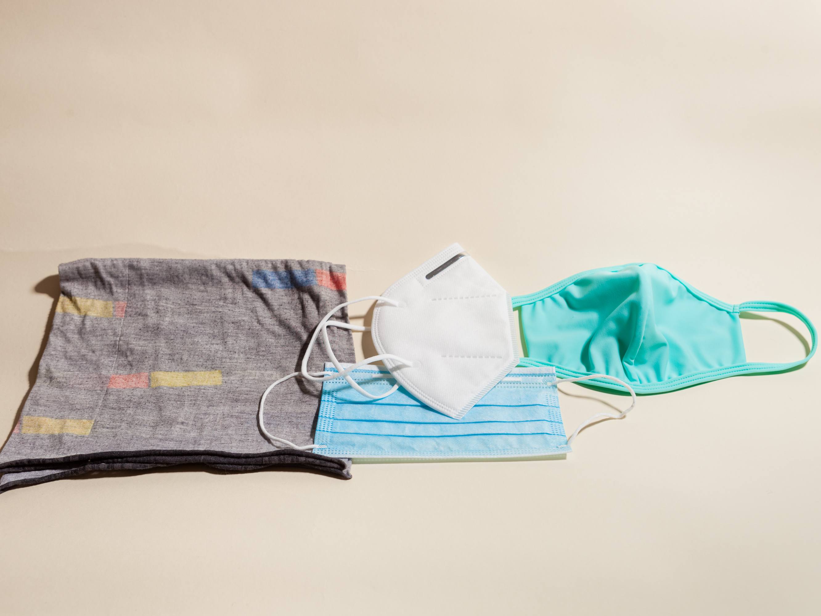 caption: Left to right: a neck gaiter (aka a buff) that slips over the head; the KN95 mask, a version of the N95 mask used in U.S. hospitals; a pleated surgical mask (below the KN95); a cloth mask.
