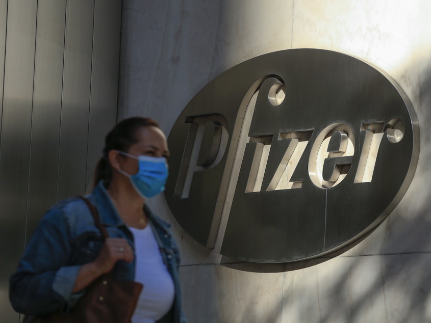 caption: A woman wears a mask as she walks by Pfizer's world headquarters in New York last month.