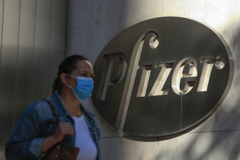 caption: A woman wears a mask as she walks by Pfizer's world headquarters in New York last month.