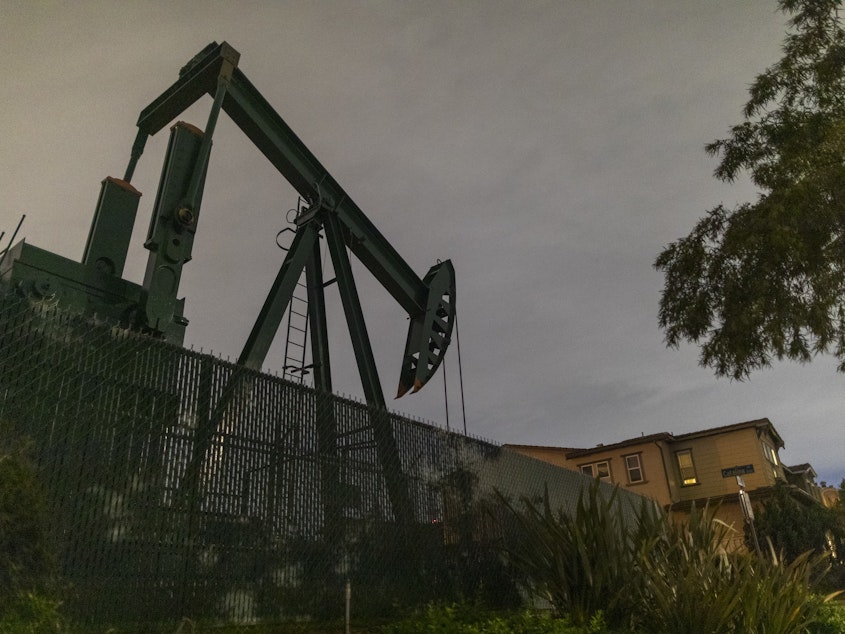 caption: Pump jacks draw crude oil from the Long Beach Oil Field near homes in Signal Hill, Calif., on March 9. The world's crude oil supply is rising even as demand is cratering.