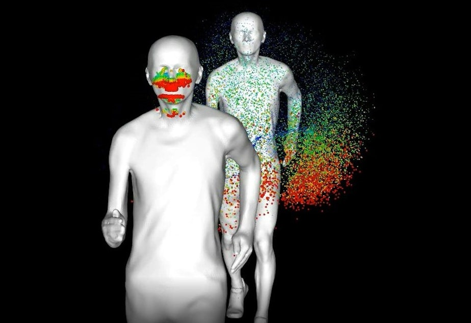 caption: Screengrab of simulation of a runner's exhalation splattering a runner behind him. Red represents the largest droplets, while blue represents the smallest.