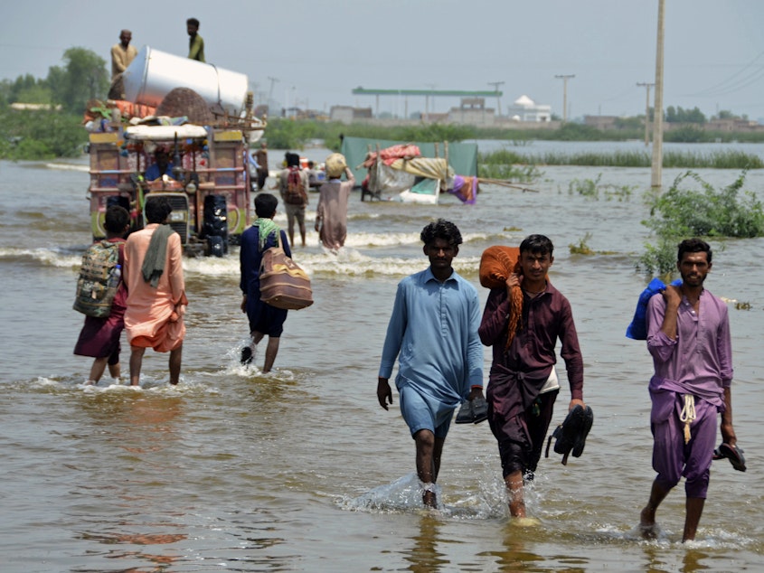 caption: People wade through a flooded area in Pakistan, that has been dealing with what people are calling "monster monsoons".
