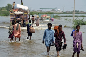 caption: People wade through a flooded area in Pakistan, that has been dealing with what people are calling "monster monsoons".