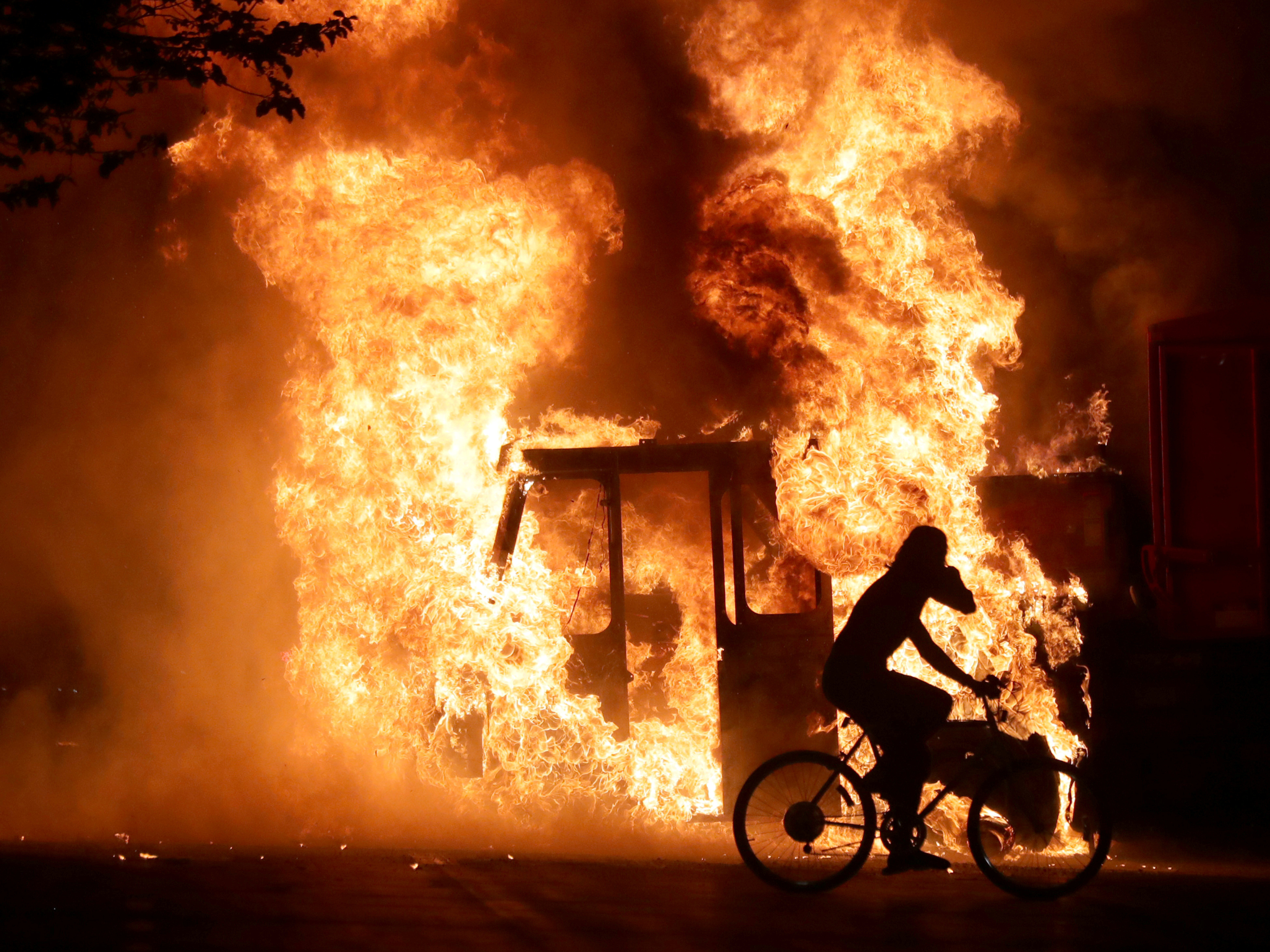caption: A man on a bike rides past a city truck on fire outside the Kenosha County Courthouse in Kenosha, Wis., during protests following the police shooting of Jacob Blake, a Black man, on Sunday.